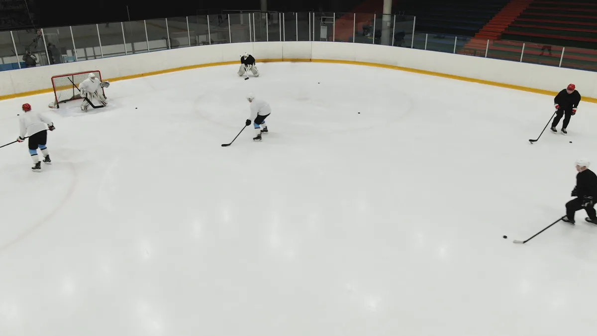 Entraînement de hockey sur glace vu du haut des gradins, gardien dans sa cage et joueurs en exercice de tir