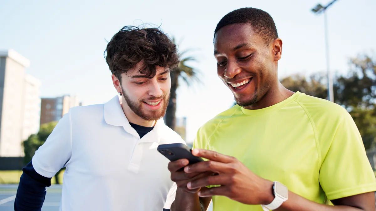 Deux joueurs sourient en regardant une vidéo sur un téléphone, au bord d'un terrain en plein air