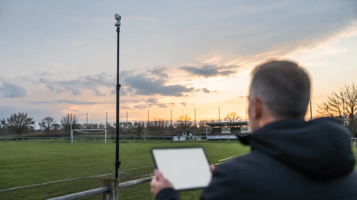 Caméra automatique en haut d'un mât au bord d'un terrain vide, un dirigeant de club regardant un devis sur une tablette