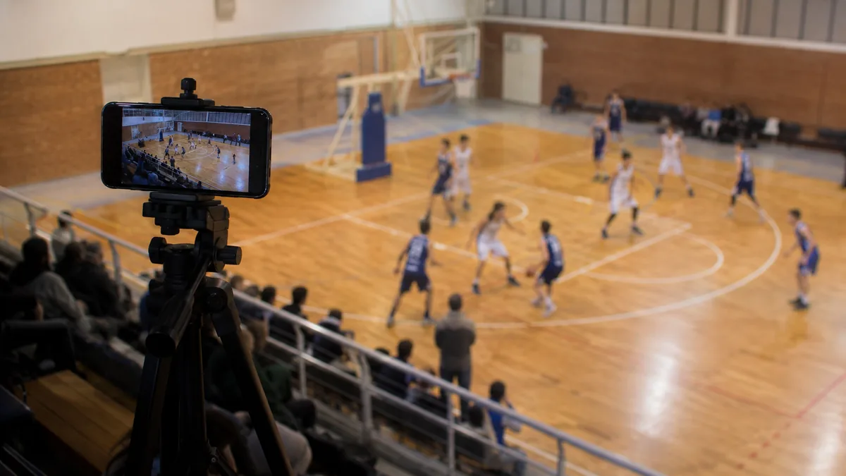 Match de basket filmé depuis le haut d'une tribune de gymnase, téléphone sur trépied