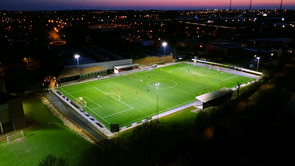 Terrain de football synthétique éclairé à la tombée de la nuit, vu de haut, un entraînement en cours au milieu de la ville